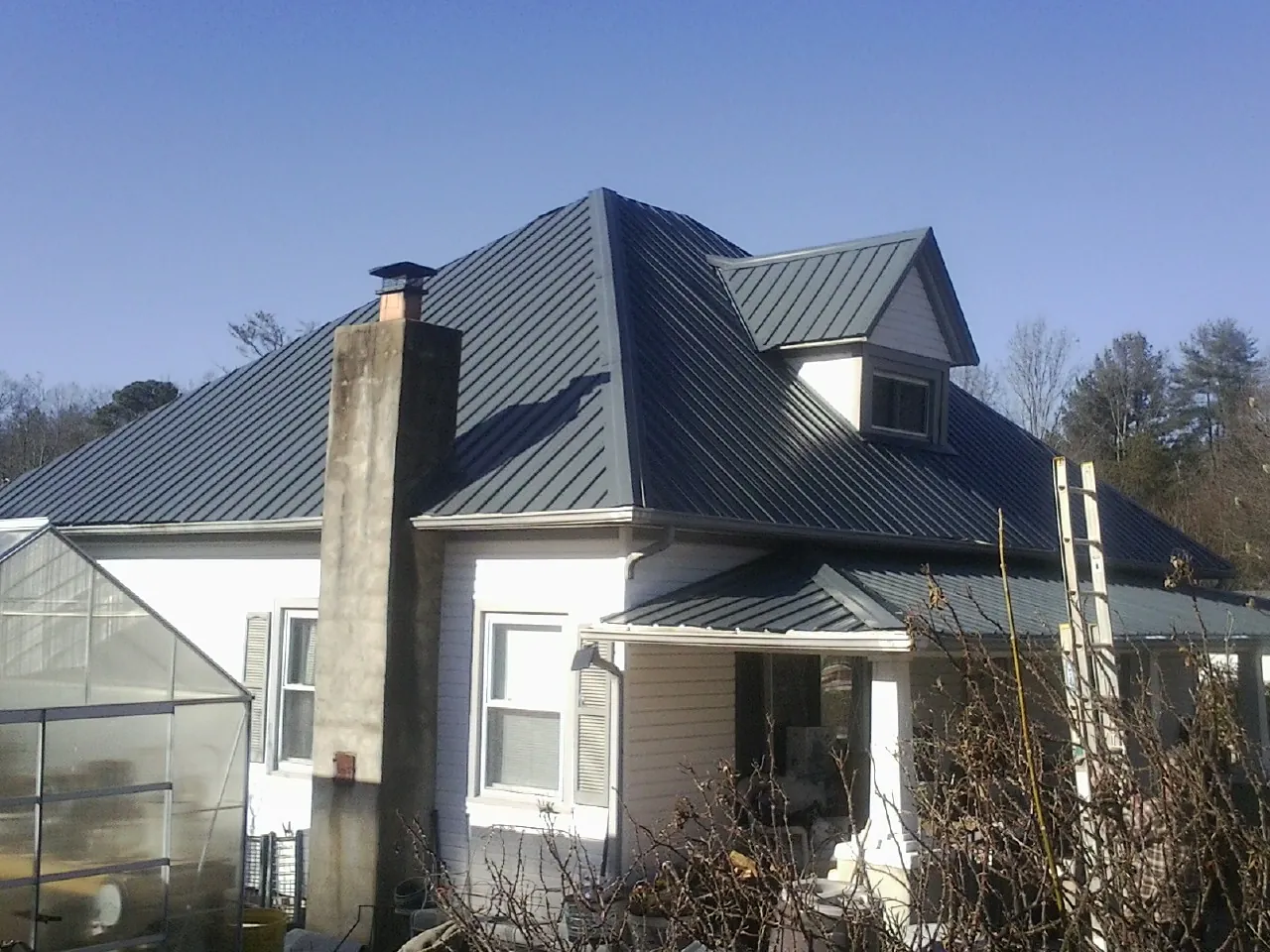 Dark blue standing seam metal roof on a white farmhouse with dormer — Slate & Tile Roof Repair by Roofing Brothers in Willington