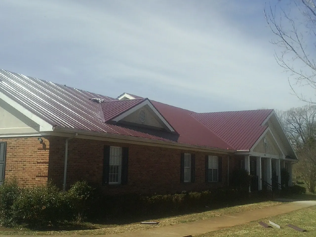 Red metal roof with gabled entries on a long brick building, from a Hail Damage Roof Repair job in Willington