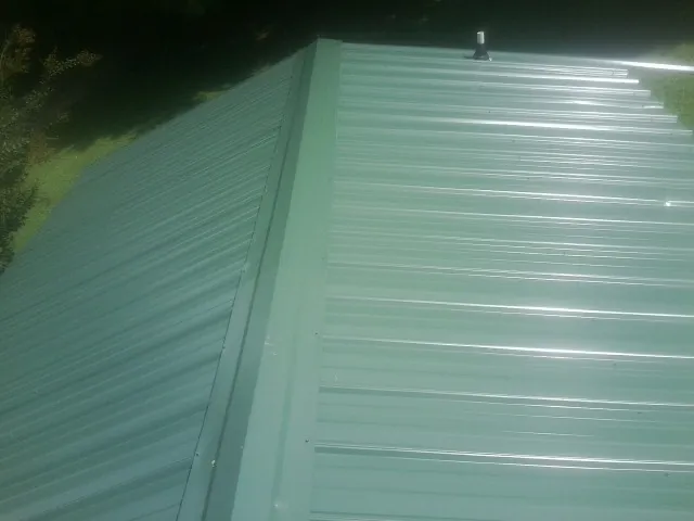 New green metal panels meeting at the ridge of a roof — Flat Roof Repair work by our crew in Willington
