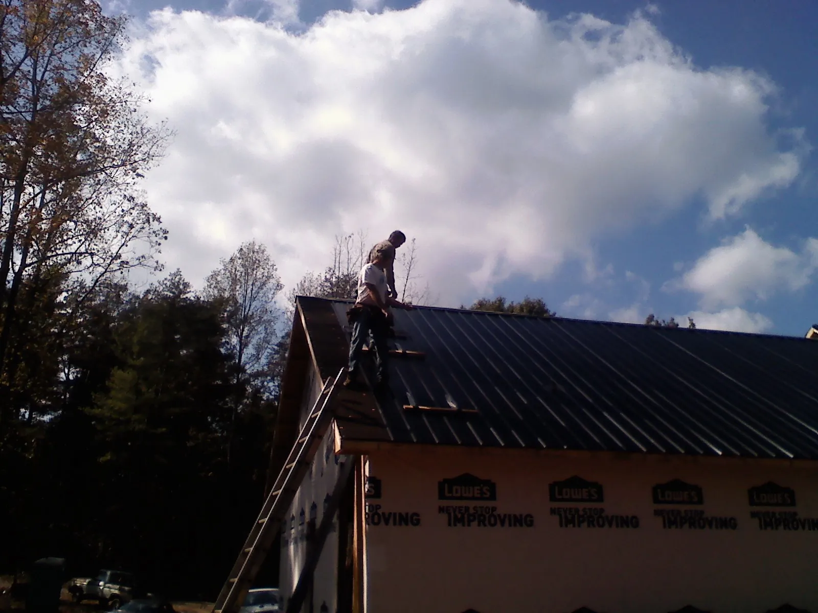 Roofer fastening dark metal panels high against a cloudy sky, from a Roof Inspection job in Willington