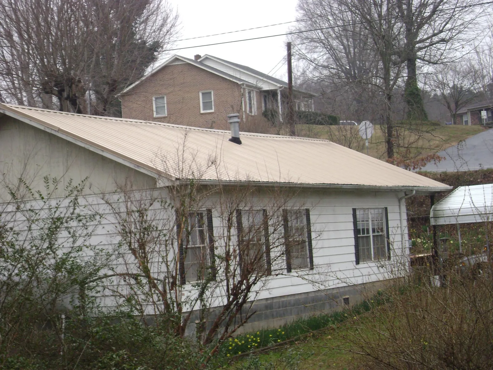 Tan metal roof on a white sided house set into a hillside — Commercial Roofing by Roofing Brothers in Willington
